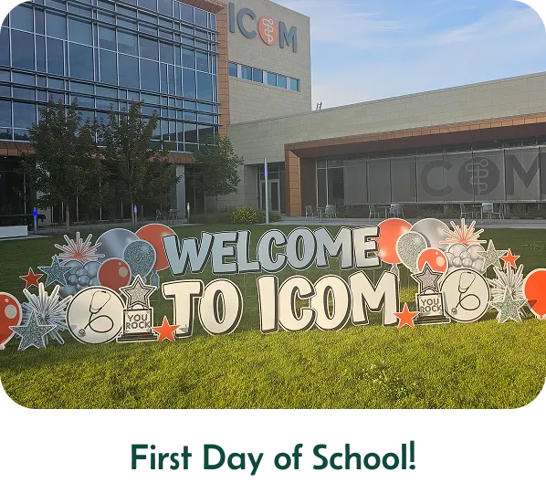 A yard sign in front of a school that says "WELCOME TO ICOM" with other graphics around it. The text below the images says "First Day of School!"
