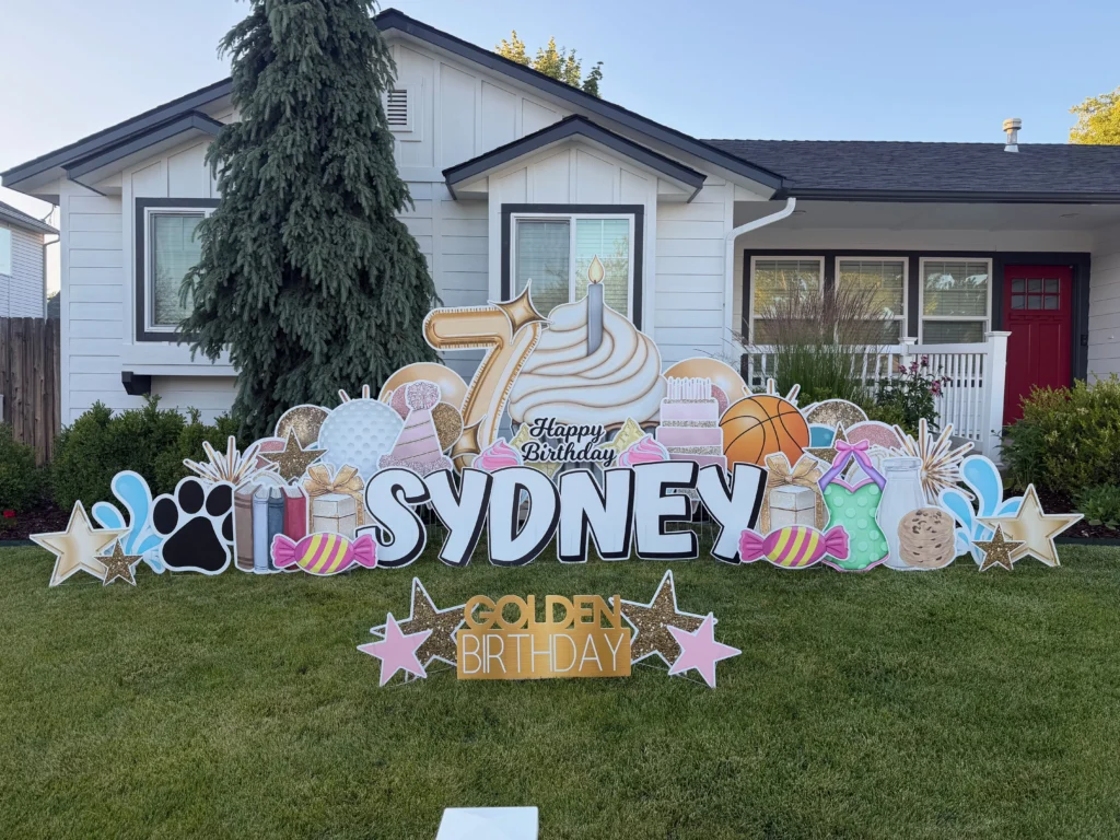 A custom yard sign in front of a house with a large number seven and a cupcake, with a phrase that says "Happy Birthday Sydney"
